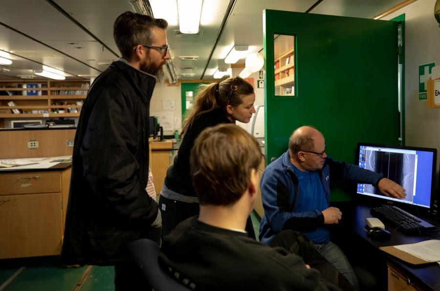 Scientists are shown tightly gathered around a computer.