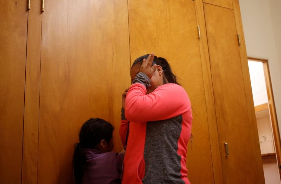 A Guatemalan woman s shown wearing a pink and grey shirt and wiping away tears. 