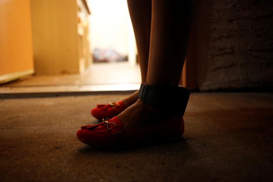 A close-up photograph of a woman wearing an ankle monitor. 