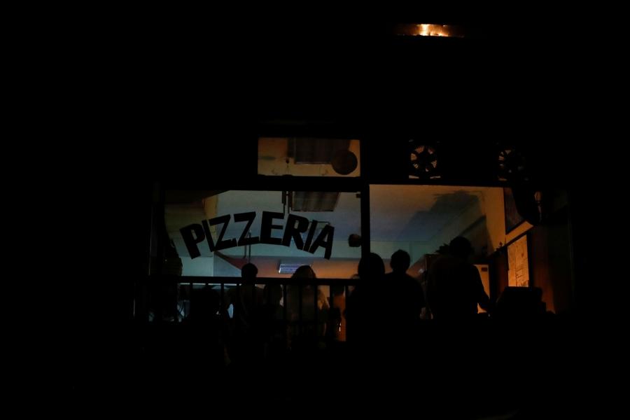 A darkened pizza shop is shown with patrons eating by candlelight.