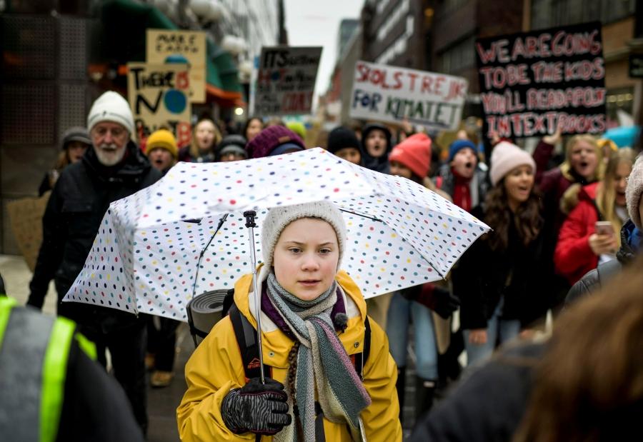 Swedish environmental activist Greta Thunberg is shown in a yellow jacket and carrying an umbrella.