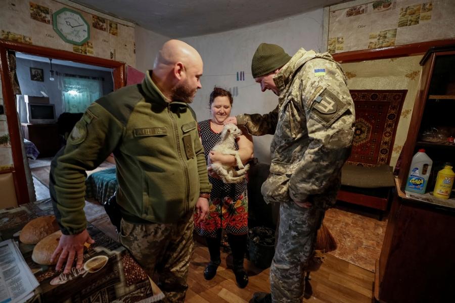 Two Ukrainian servicemen are shown on either side of a woman holding a small goat. 