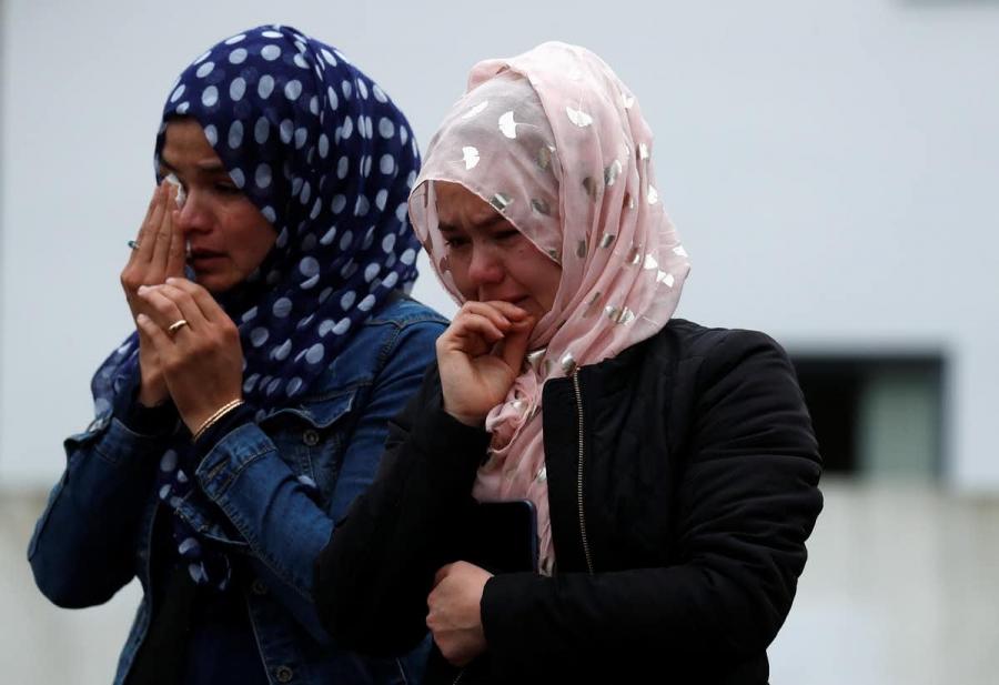 two women wearing hijab cry into their hands 