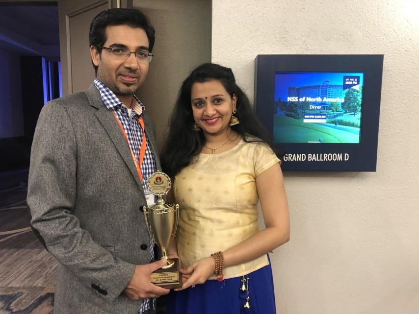 A man and a woman hold a trophy in a hotel hallway