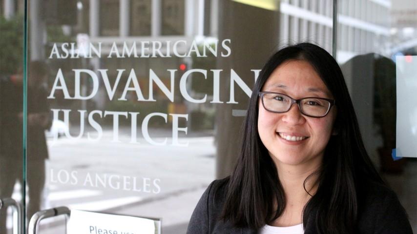 A woman with glasses stands in front of an office front with the sign Asian Americans Advancing Justice Los Angeles