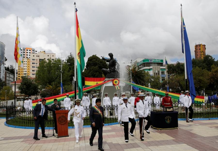 The president of Bolivia stands in front of a podium and behind him is the Bolivian navy, dressed in white. 