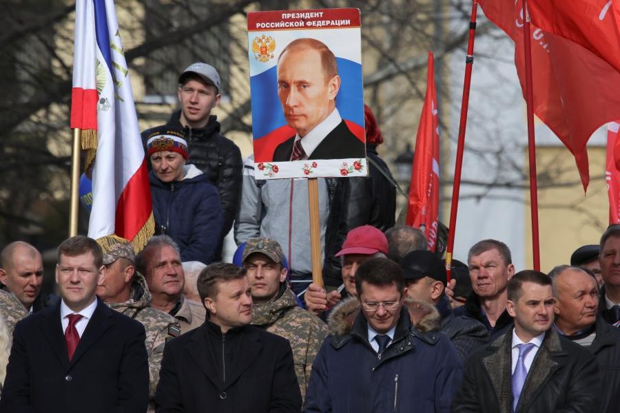 A man holds a board with a portrait of Russian President Vladimir Putin surrounded by other men