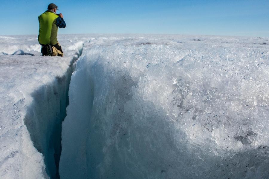 University of Montana glaciologist Joel Harper is shown knealing next to a deep crack in the ice sheet called a crevasse.