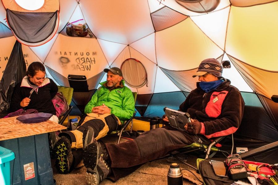 The crew gathered is shown lounging in chairs for meals in a tent on the ice.