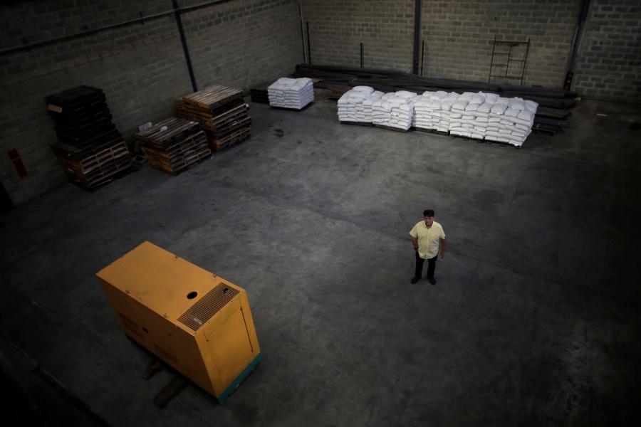In a photograph taken from above, a man in a yellow shirt is shown standing in a nearly empty warehouse.