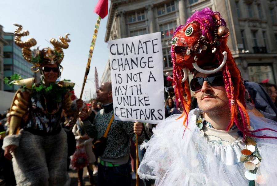 A man with a mask in a crowd of protesters. Someone holds a sign reading: Climate change is not a myth unlike centaurs.