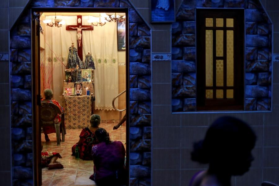 Women kneel before a cross, seen through a doorway