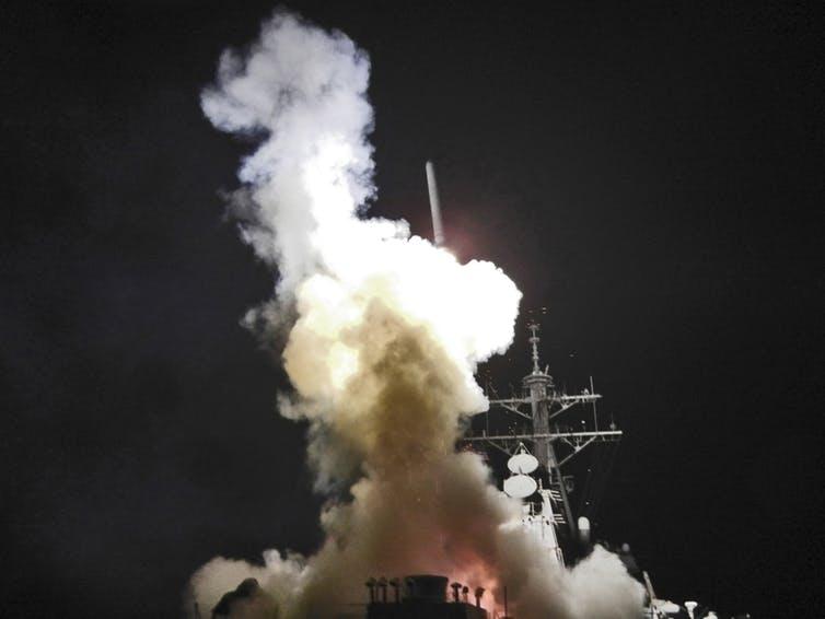 Smoke fills the air as a missile is launched from a military boat at night. 