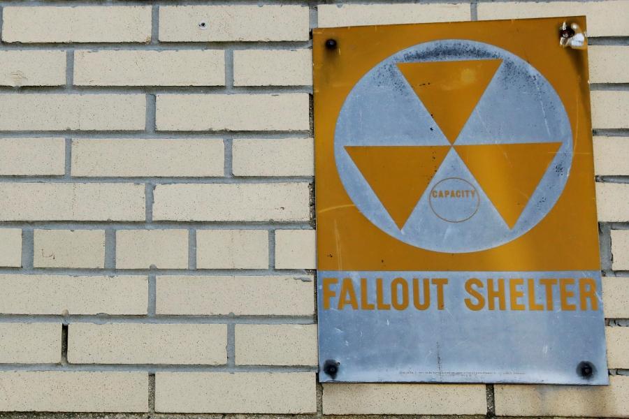A yellow nuclear fallout shelter sign is seen hung on a brick building