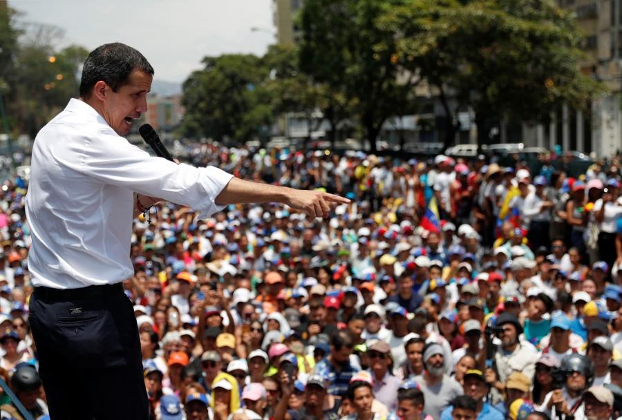 Venezuelan opposition leader Juan Guaidó is shown in a white shirt and holding a microphone while gesturing to supporters