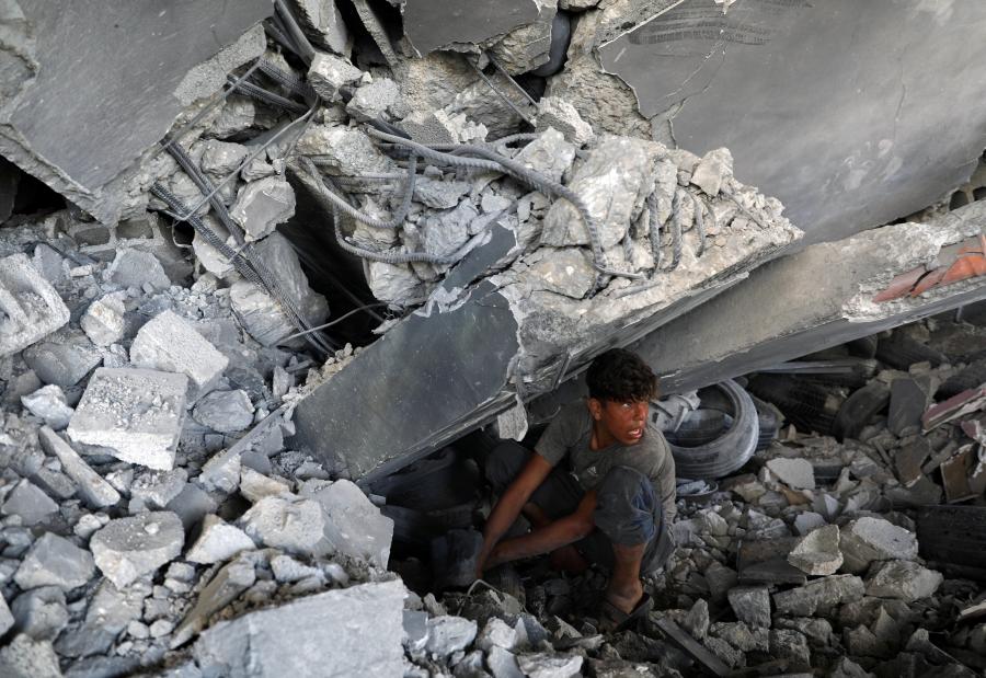 A boy squats in building rubble