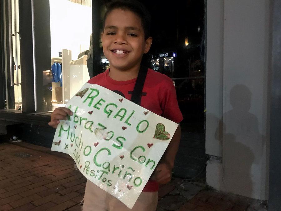 A young boy holds a sign selling hugs for 100 pesos