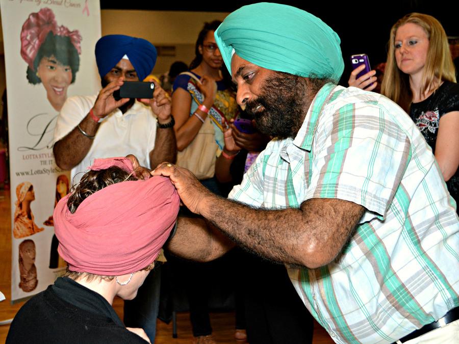 A crowd gathers around a Sikh man who is showing how to wrap a dastar or turban. 