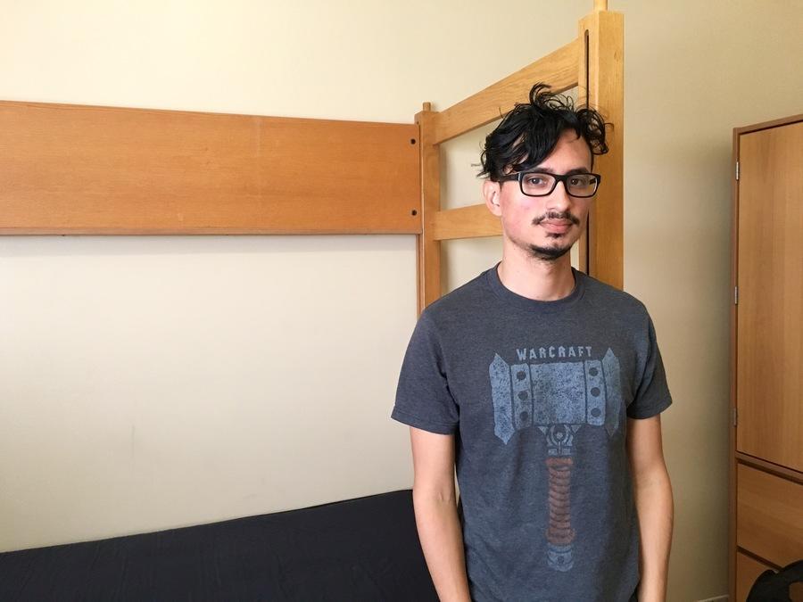 Man stands in front of a bed in a dorm room