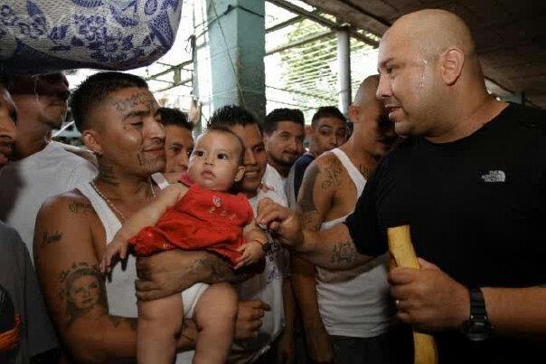 Man with tattoos holding baby, talking to another man in black T-shirt
