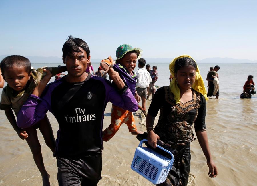 A Rohingya refugee man holding children walks towards the shore