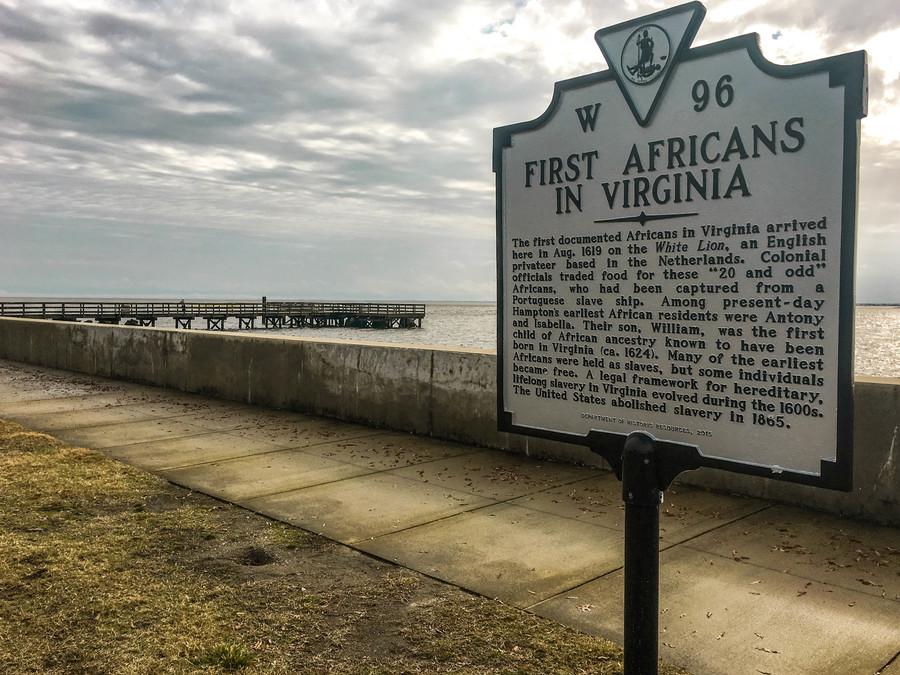 A sign marking the arrival of the first enslaved Africans in front of a seascape. 