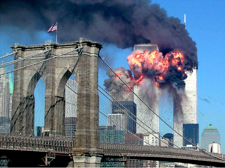 The second tower of the World Trade Centre explodes after being hit by a hijacked airplane. A bridge with an American flag flying is in the foreground. 