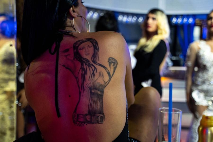 A tatoo is shown on the back of a person in dark outline showing a woman with long hair and her arm raised.