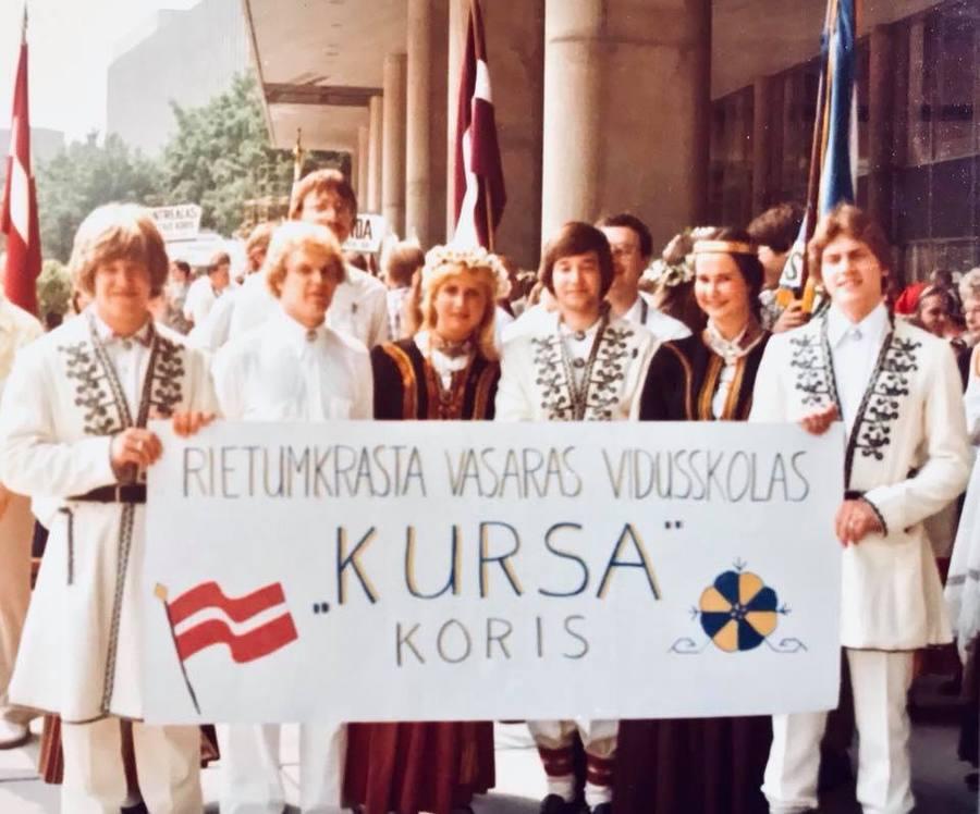 An archival photo of teenagers in folk costumes holding a sign