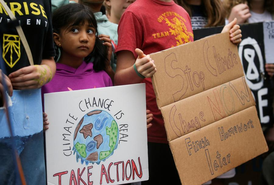 A young girl holds a sign reading "climate change is real, take action" among other young protesters.