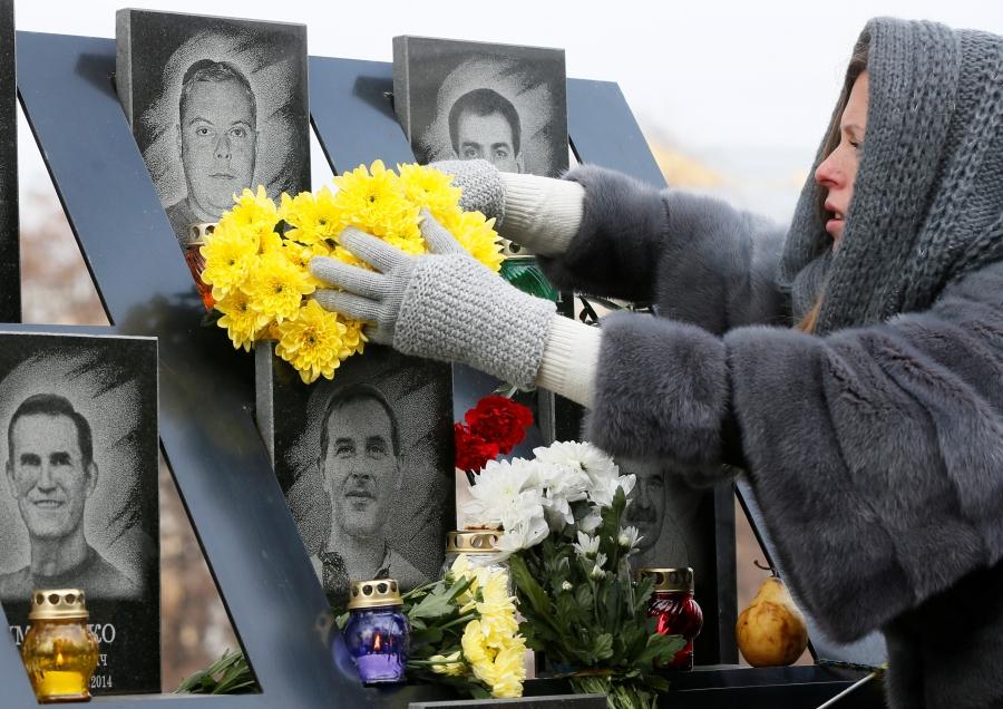 A woman lays flowers during a commemoration ceremony in front of a monument with images of men