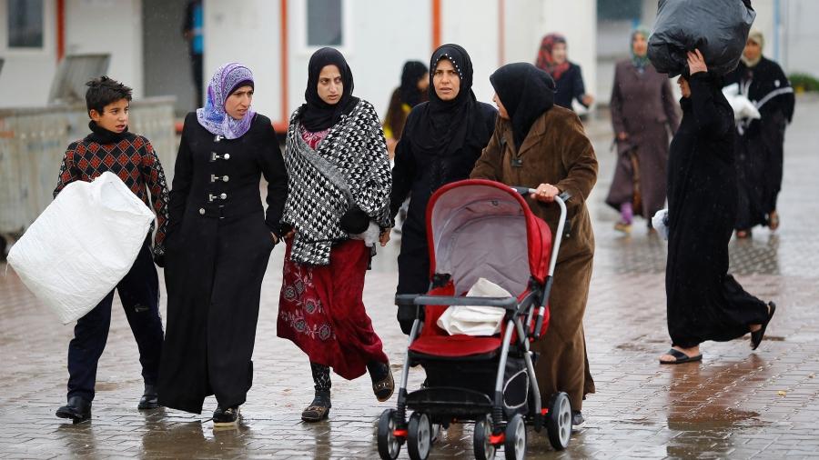 Syrian refugee women walk and push a stroller