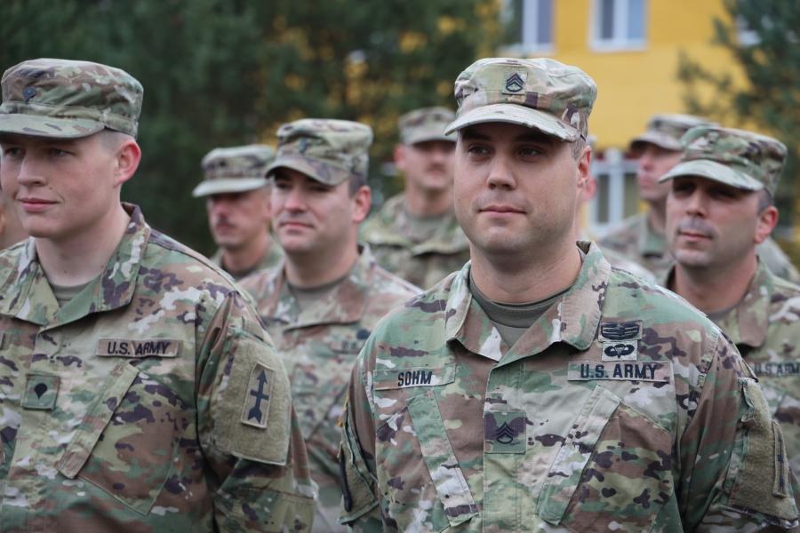 focus on a mid-shot of a man in US Army uniform with others around him. 