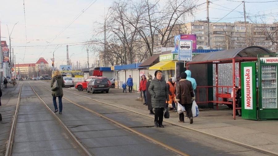 A tram line cuts through a suburban neighborhood in Kyiv, Ukraine, as people walk on the street.