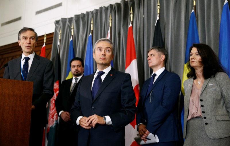 Several people stand in suits in front of flags. 