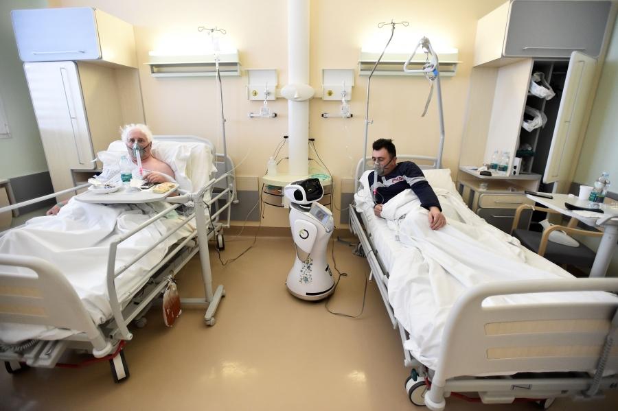 Two patients wear oxygen masks in a hospital and look at a small robot.