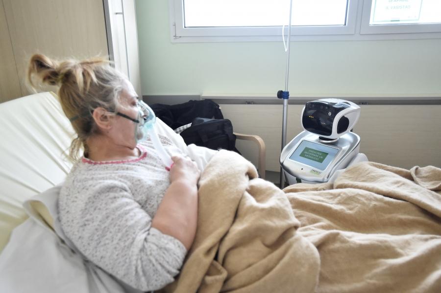 A sick woman looks at a robot from her hospital bed.