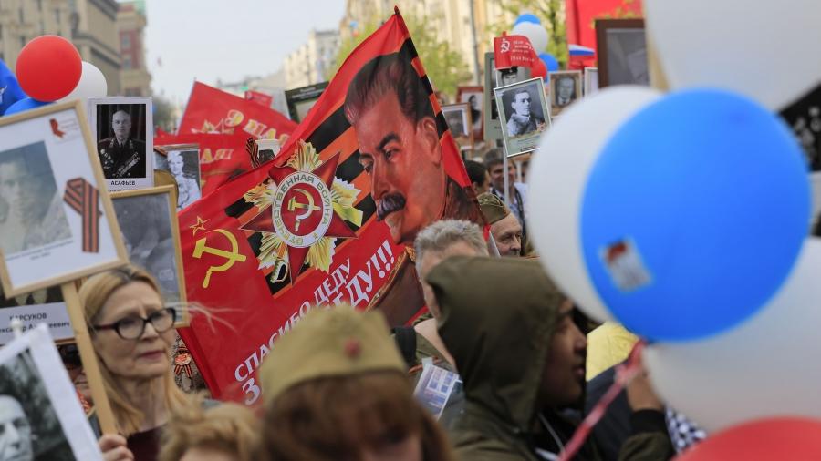 A crowd of people hold balloons, photos and a banner of Joseph Stalin
