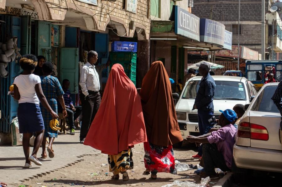 Two women wearing long colorful robes and hijab walk down a street in the Eastleigh area of Nairobi, Kenya. 
