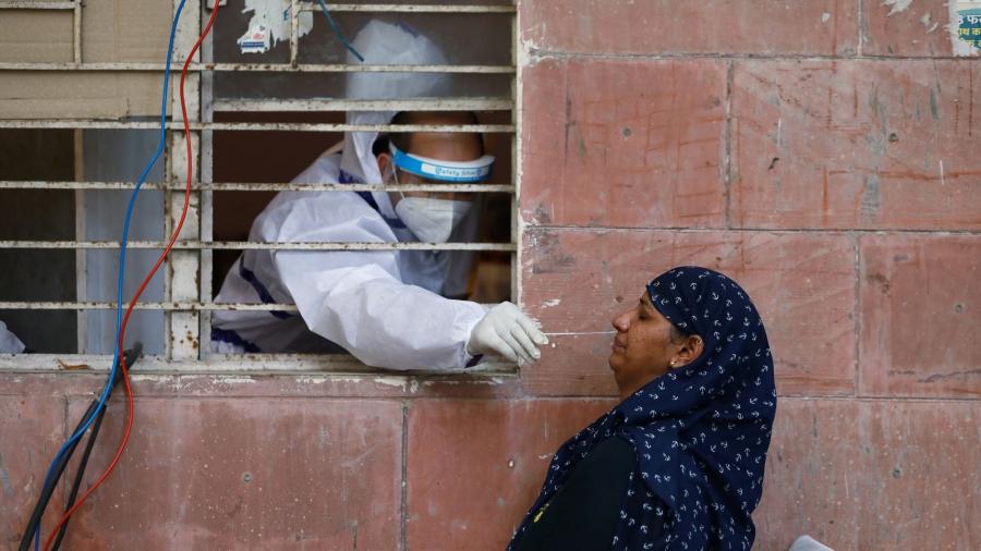 A medical worker is shown reaching through a window with bars on it while wearing protective medical gear and a women outside being tested for the coronavirus.