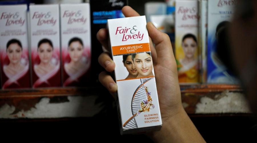 Skin lightening creams are exhibited on a shelve while a holds one cream in her hand.