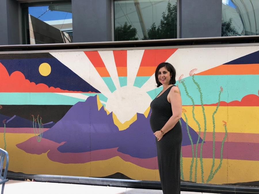 Woman in black sleeveless dress poses in front of a colorful painting