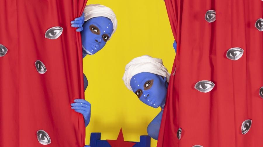 Close-up of Aïda Muluneh's "The Weakness of Power" shows 2 women with their faces painted blue looking at the camera from behind red curtains.