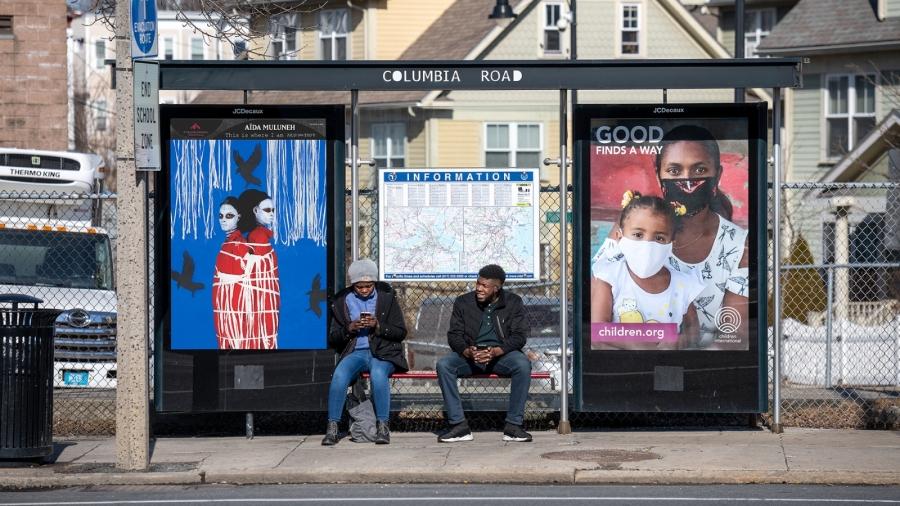 Aïda Muluneh's "The faith of fate" is shown at a bus stop in the Boston area as two people wait for transportation.