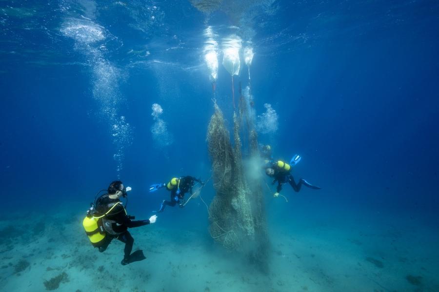 Divers underwater cleaning up discarded fishing nets stuck in the water