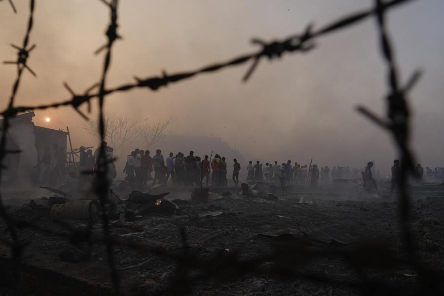Foggy photo from behind a fence of refugees walking around a camp after a major fire