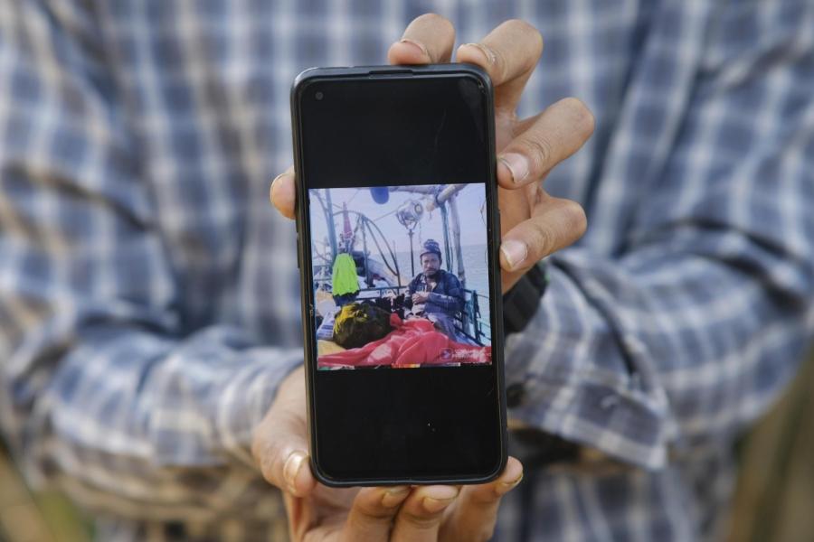 A person holding their cellphone and showing a photo of a man sitting on a boat.