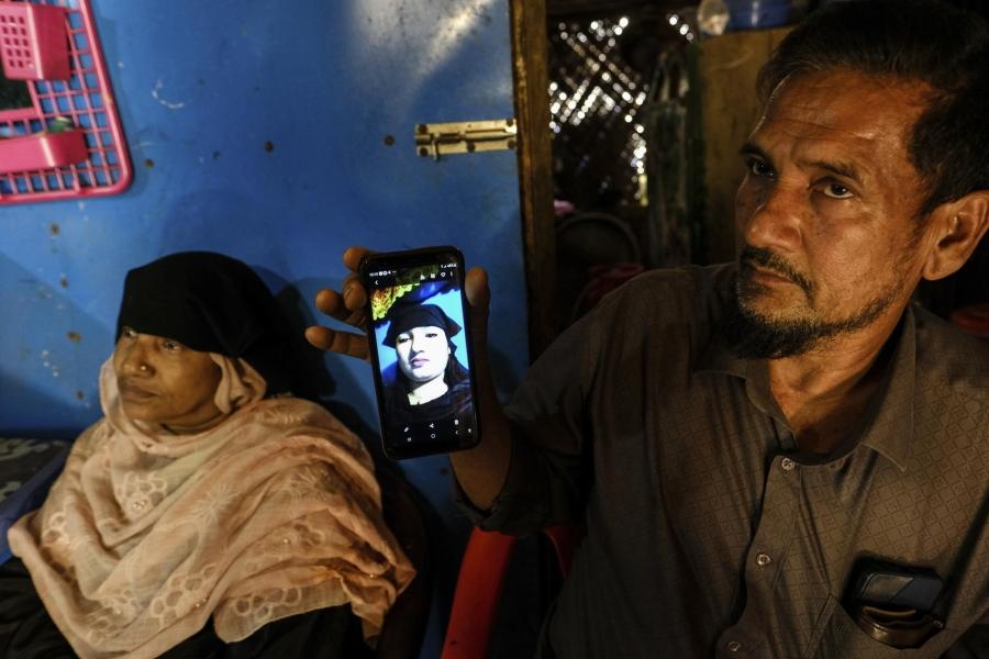 A man and woman sitting next to each other while a man holds up his cell phone that shows a picture of his daughter