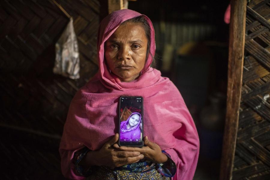A woman standing in a pink hijab holding a cellphone with the image of a loved one