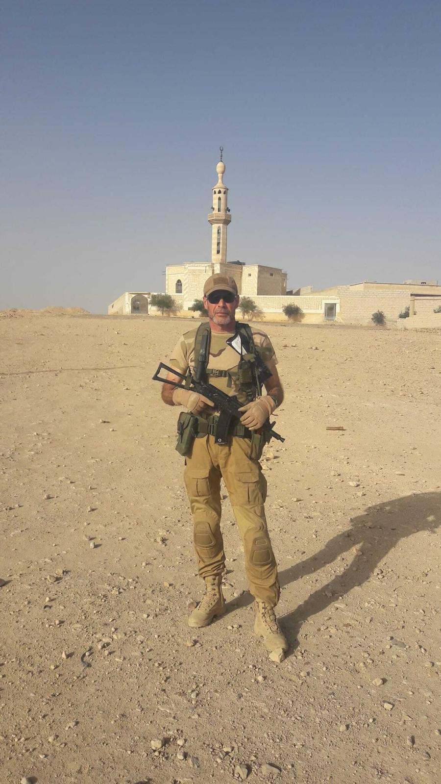 a man standing in the desert holding a gun in a military uniform